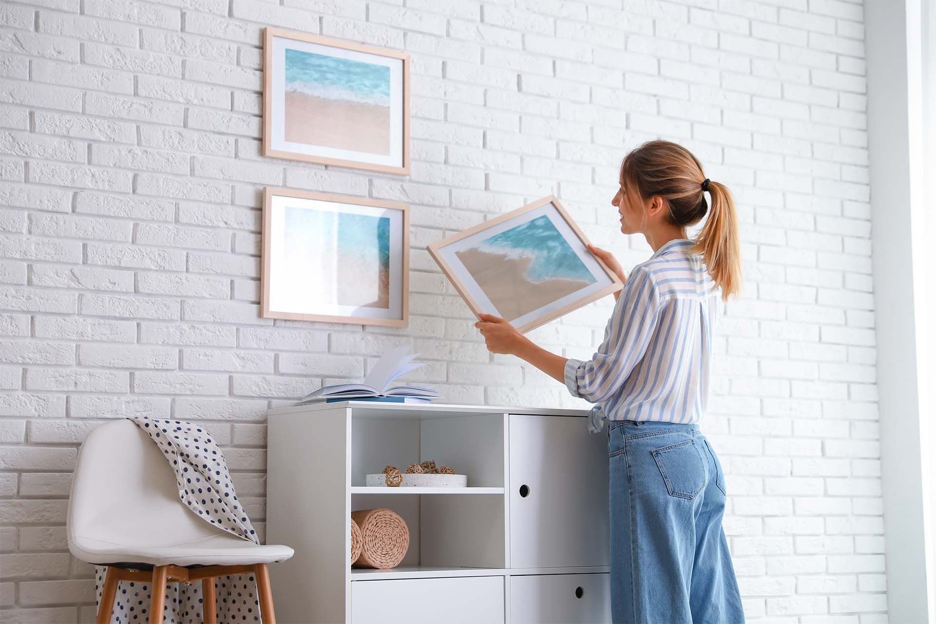 Jeune femme qui accroche des peintures sur son mur de briques